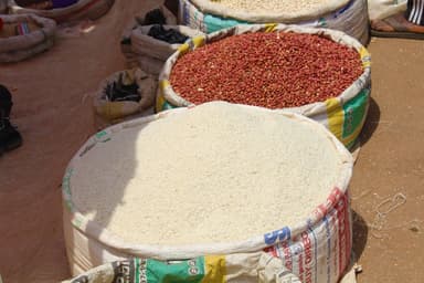An open sack of rice beside a sack of groundnuts at a market stall